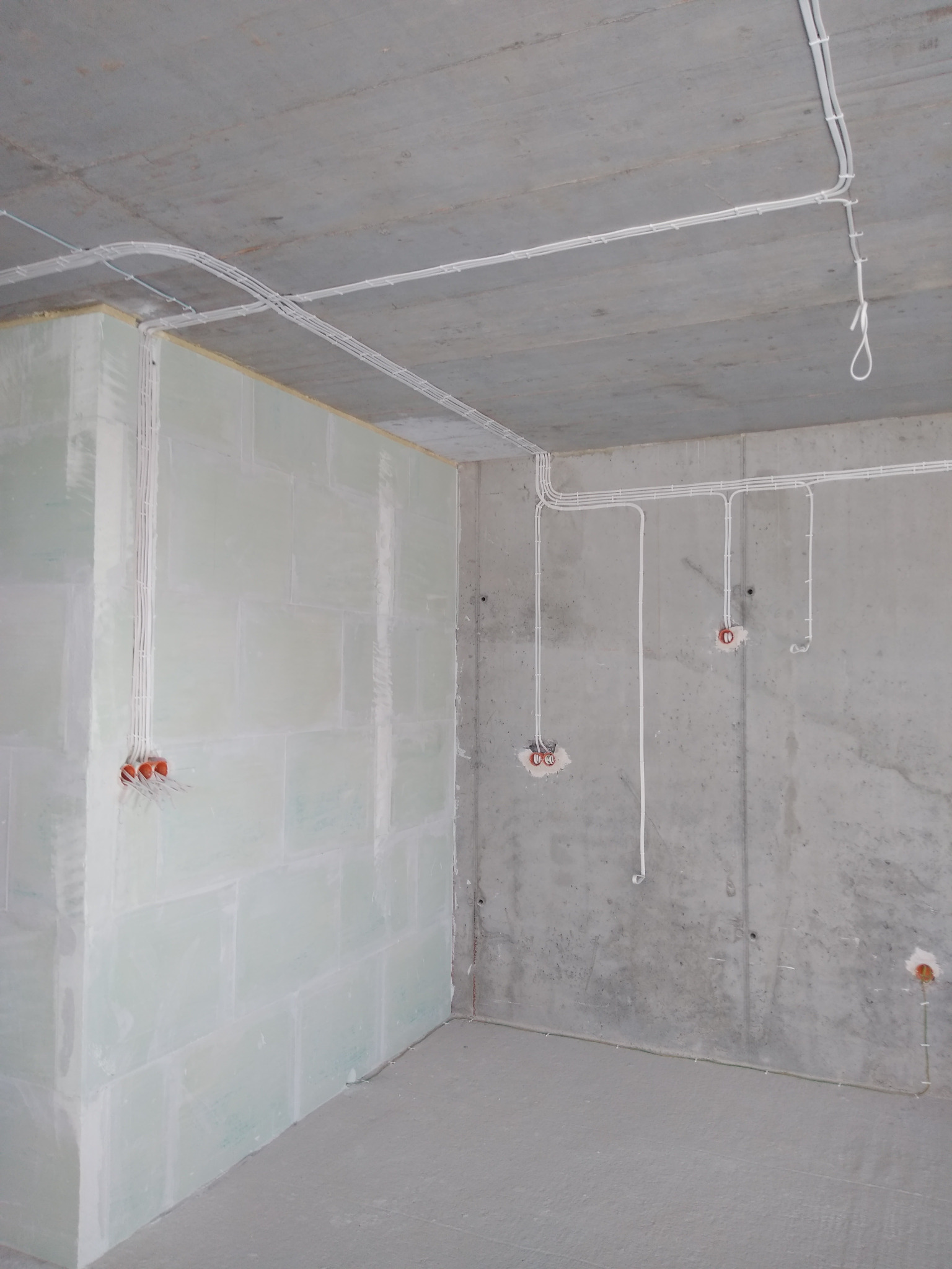 Surowe wnętrze w trakcie prac elektrycznych: widoczne kable prowadzone po ścianach i suficie, puszki instalacyjne w ścianach, surowy beton i płyty gipsowe.