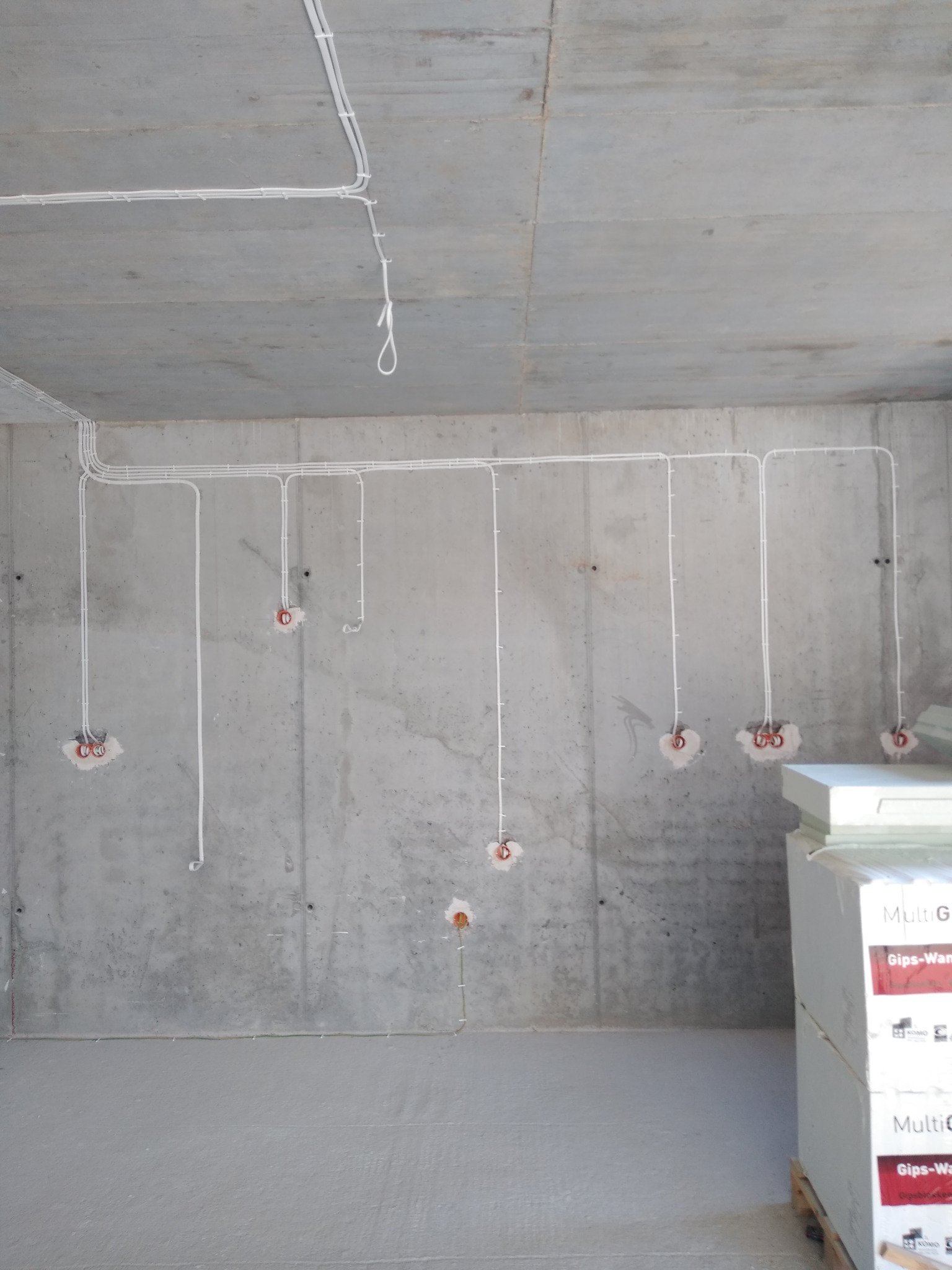 Surowy beton i białe kable elektryczne w nowym budynku. Widoczne puszki instalacyjne i fragmenty izolacji. Minimalistyczny kadr z instalacją.