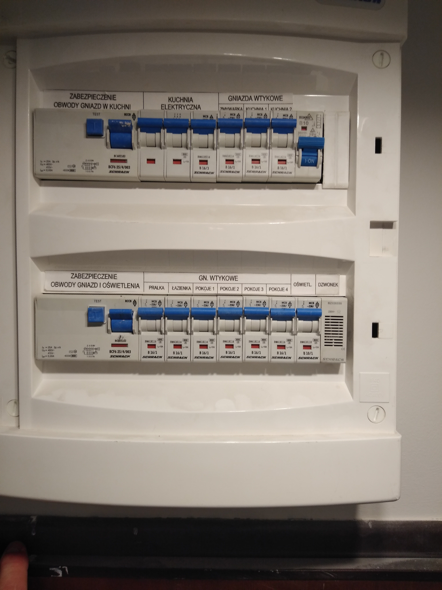 Rozdzielnica elektryczna Schrack z bezpiecznikami oznaczonymi dla obwodów gniazd w kuchni, gniazd wtykowych, oświetlenia i innych pomieszczeń. Widoczne oznaczenia i parametry.