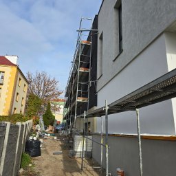 Przemek Najlepszy - Budynek w trakcie prac wykończeniowych elewacji, widoczne rusztowania, fragmenty otynkowanej ściany z oknami, przygotowany teren wokół budynku.