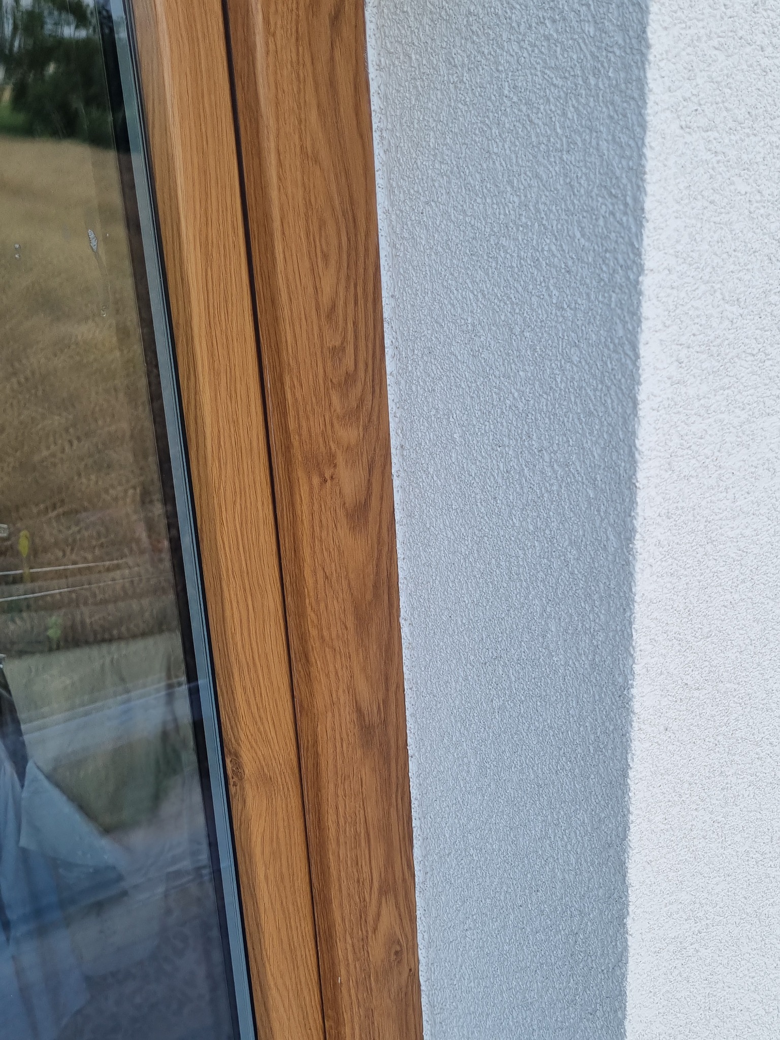 Fragment elewacji z oknem o drewnianej ramie; widoczna struktura tynku w dwóch odcieniach szarości.