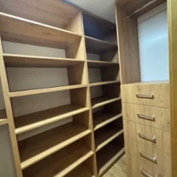 Jasna, drewniana garderoba z otwartymi półkami i szufladami, widok z dołu, minimalistyczny design.