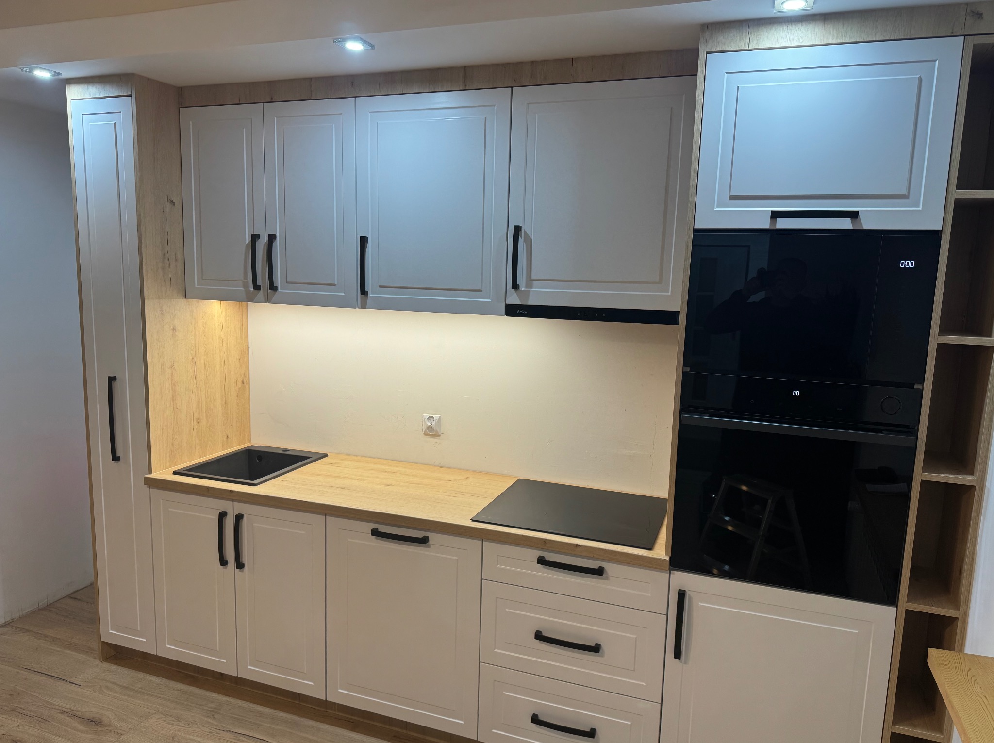 Nowoczesna kuchnia z białymi frontami szafek, drewnianym blatem i wbudowanym sprzętem AGD: piekarnikiem i płytą indukcyjną.