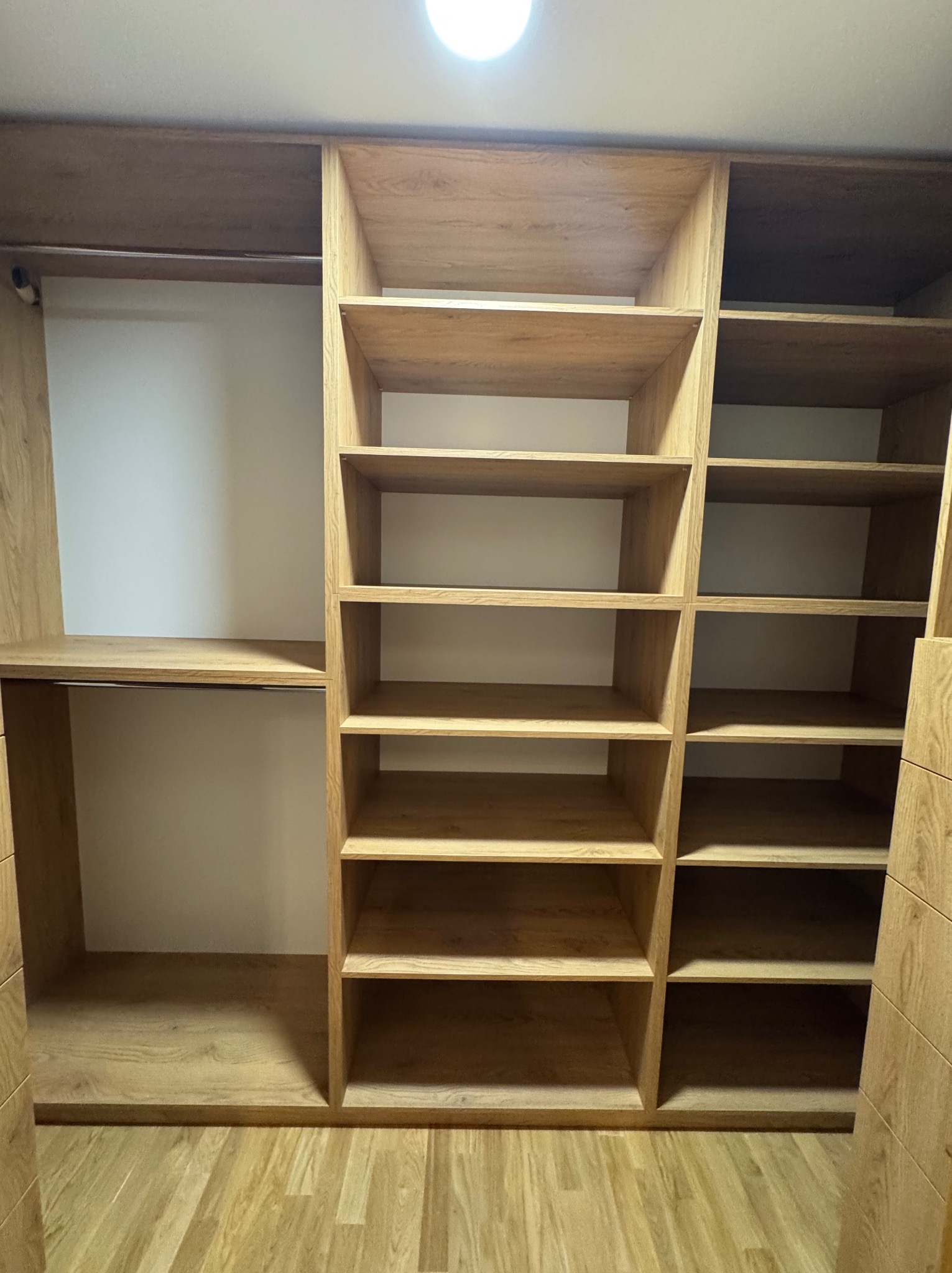 Wnętrze szafy wnękowej z jasnego drewna z licznymi półkami i drążkiem na ubrania, widok z dołu.