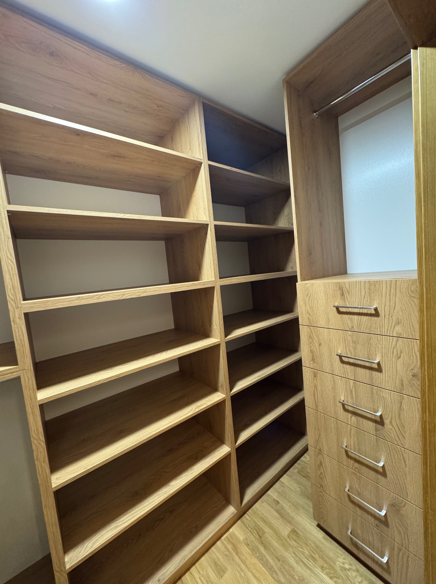 Jasna, drewniana garderoba z otwartymi półkami i szufladami, widok z dołu, minimalistyczny design.