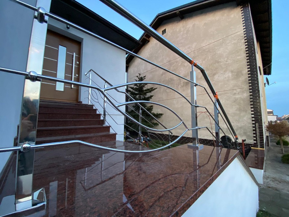 Polerowana balustrada ze stali nierdzewnej z motywem liści na schodach wejściowych z granitu, odbicie w powierzchni, nowoczesny design.