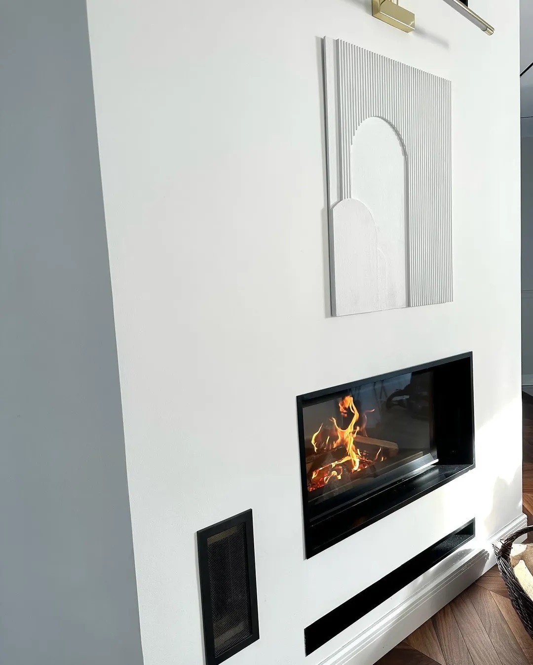 Wnętrze z nowoczesnym biokominkiem w zabudowie, ozdobnym panelem ściennym i kratką wentylacyjną, minimalistyczny design.