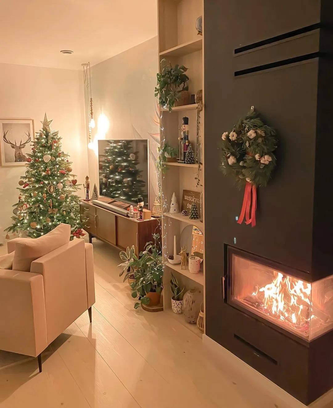 Nowoczesny czarny wkład kominkowy z paleniskiem, ozdobiony świątecznym wieńcem z czerwoną wstążką, w tle choinka i elementy wystroju wnętrza w świątecznym klimacie.