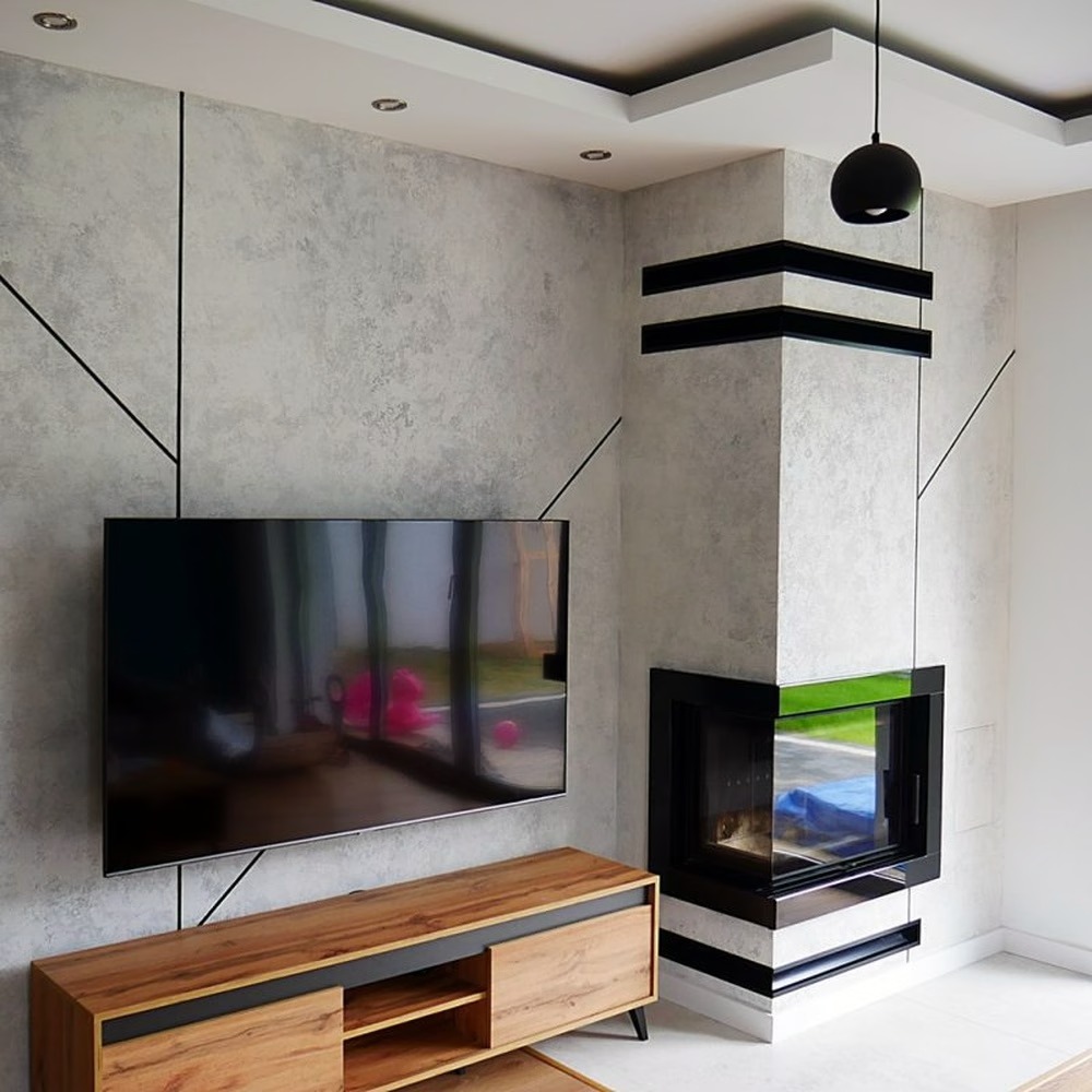 Nowoczesny salon z narożnym wkładem kominkowym obudowanym szarym kamieniem, czarne akcenty dekoracyjne i wisząca lampa, drewniana szafka RTV pod telewizorem.