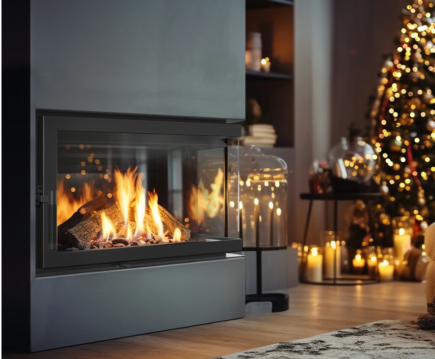 Nowoczesny, narożny kominek z paleniskiem, otoczony szkłem, w salonie z choinką. Widoczne płomienie i detale wykończenia. Oświetlenie tworzy ciepłą atmosferę.