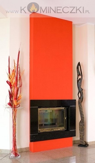 Nowoczesny kominek z czarną obudową i pomarańczowym wykończeniem, uzupełniony dekoracjami: wysokim wazonem z kwiatami i rzeźbą.