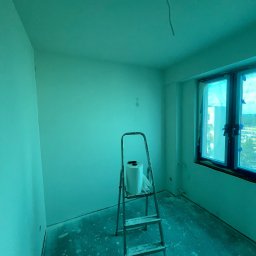 ProHome Sebastian Sulewski - Pokój po świeżym malowaniu na zielono, z drabiną i rolką malarską. Okno zabezpieczone folią. Widoczne ślady farby na podłodze.
