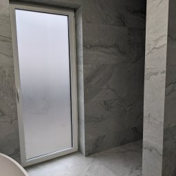 Bariev Andrzej - Nowoczesna łazienka wykończona płytkami imitującymi marmur, z oknem z matową szybą i fragmentem wolnostojącej wanny.