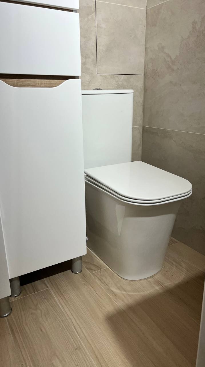 Nowoczesna toaleta w zabudowie, z szafką łazienkową i płytkami imitującymi kamień na ścianie.