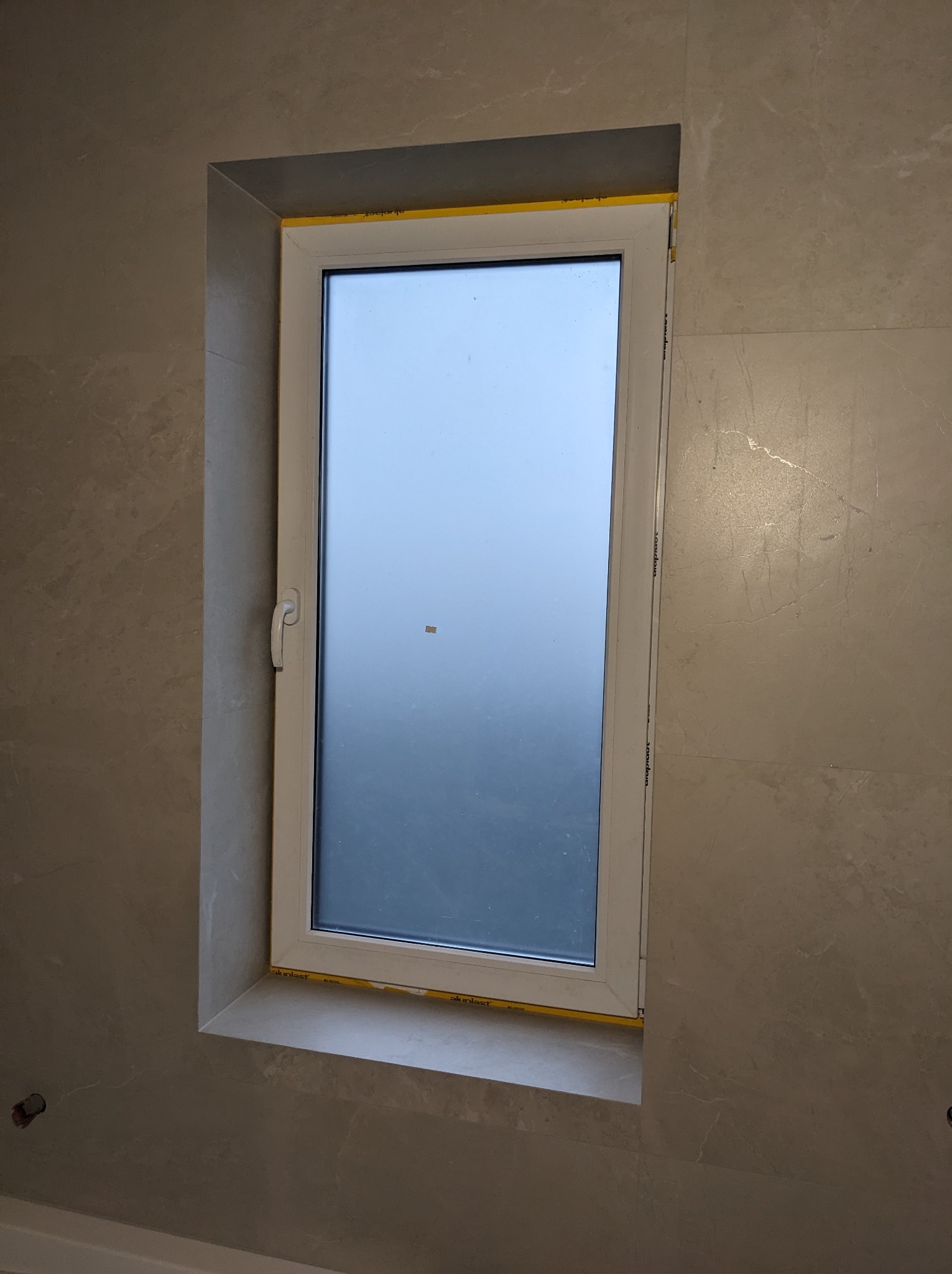 Okna PCV zamontowane we wnęce wyłożonej płytkami w łazience we Wrocławiu, widoczne ślady po taśmie zabezpieczającej na ramie okiennej.