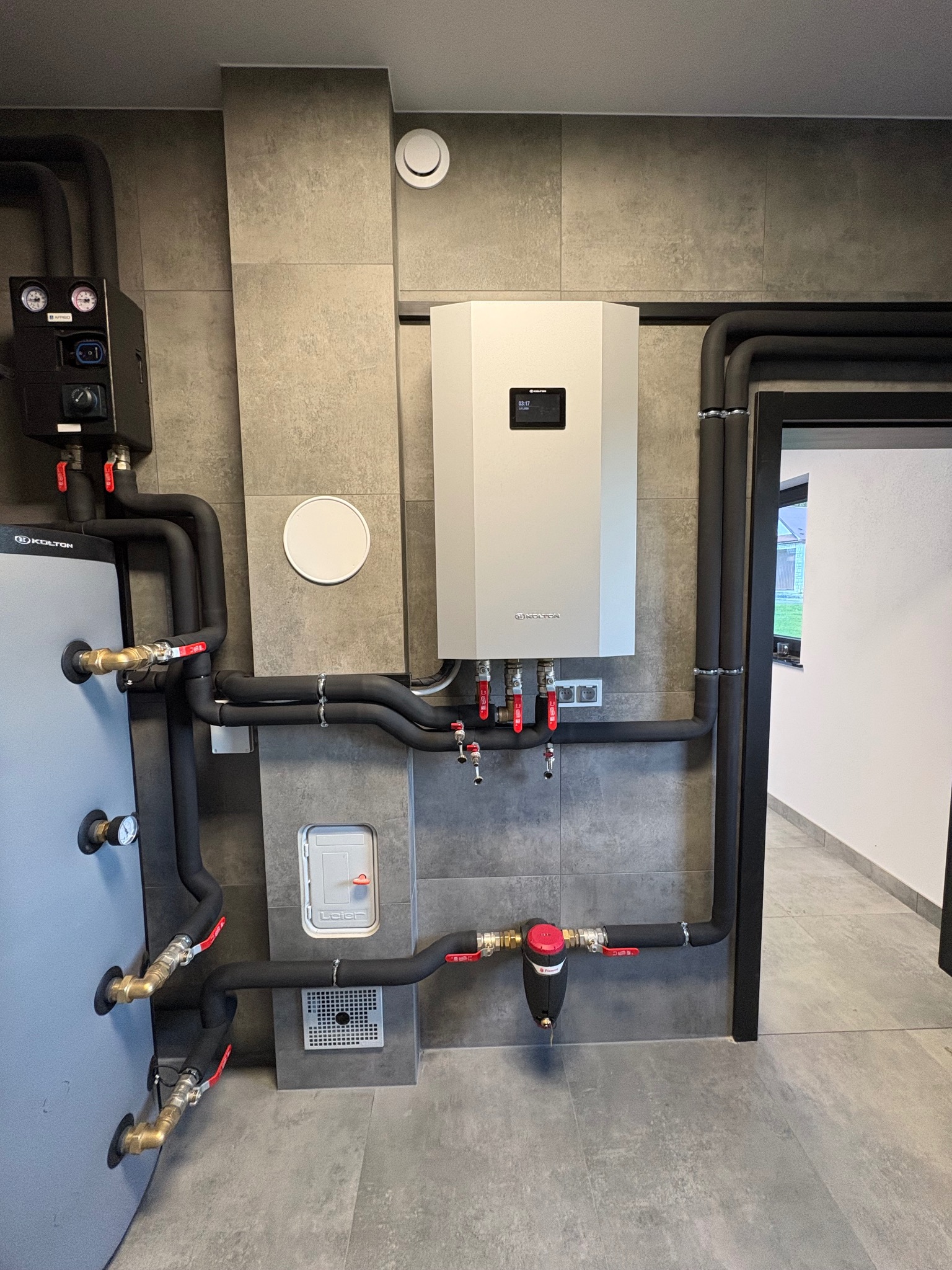 Nowoczesna kotłownia z szarymi płytkami, piecem gazowym i zbiornikiem, czarne rury z izolacją, zawory z czerwonymi uchwytami. Minimalistyczny design, schludne wykończenie.