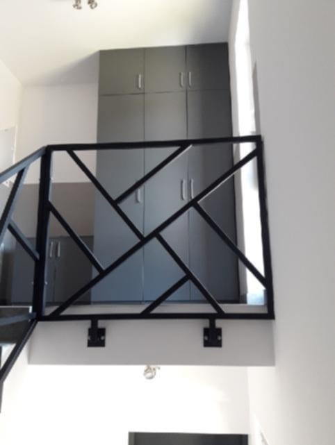 Nowoczesna, czarna balustrada metalowa o geometrycznym wzorze, zamontowana wewnątrz budynku. W tle widoczne szare szafy wnękowe i białe ściany. Minimalistyczny design.