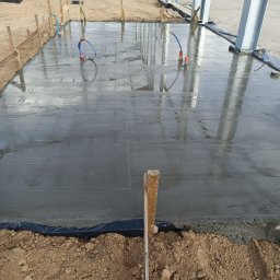 Perfect House - Wylany, mokry beton na fundamencie z widocznymi rurami instalacyjnymi i drewnianym szalunkiem, przygotowany pod budowę hali stalowej.