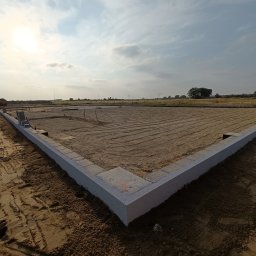 Perfect House - Fundamenty domu jednorodzinnego w trakcie budowy, z widocznym zarysem ścian i podsypką piaskową, na tle zachodzącego słońca i pól.