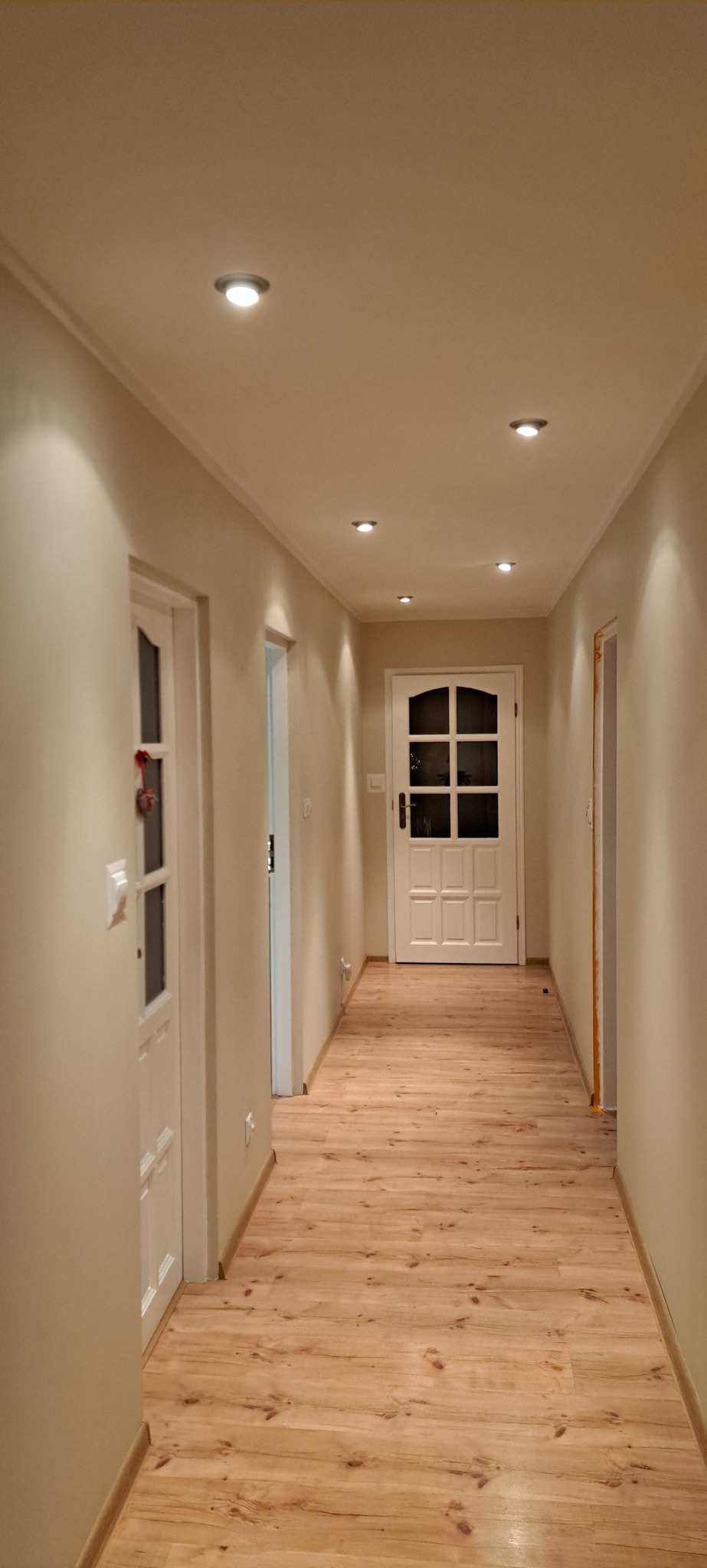 Korytarz po remoncie z drewnopodobną podłogą, białymi drzwiami i oświetleniem sufitowym punktowym.