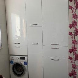 MatWood Design - Biała szafa na wymiar z połyskiem, zabudowa pralki w łazience, chromowane uchwyty, płytki z motywem kwiatowym po prawej stronie. Nowoczesny design.