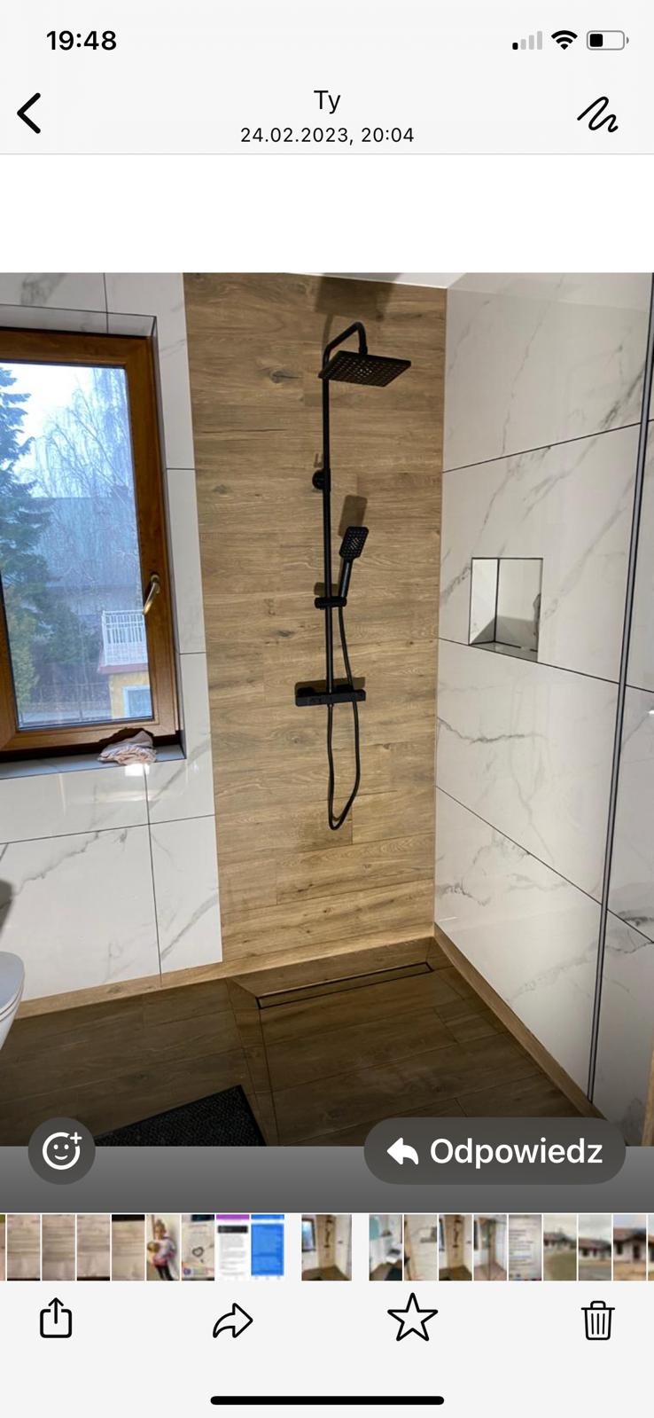 Wykończona łazienka z kabiną typu walk-in, wyłożona płytkami imitującymi drewno i marmur, z czarną armaturą. Widoczne okno z widokiem na zewnątrz.