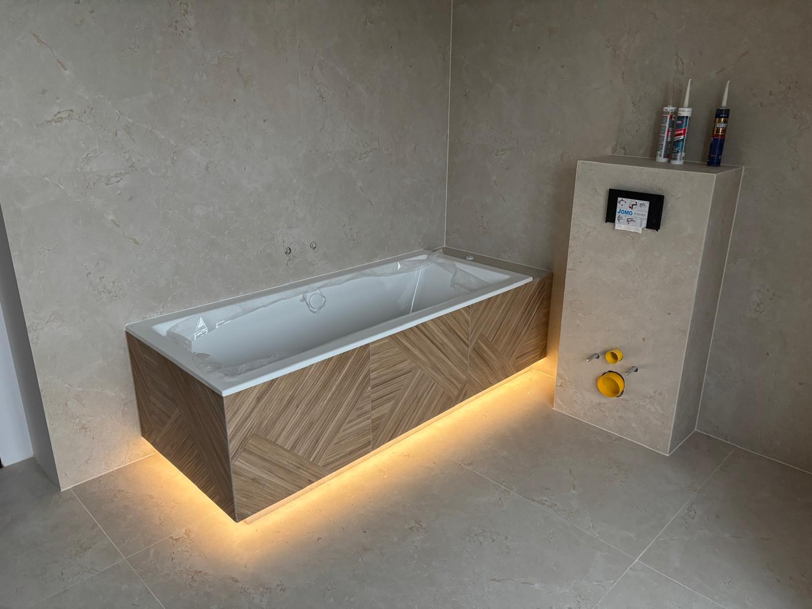 Nowoczesna zabudowa wanny z podświetleniem LED i obudowa stelaża WC w łazience w Białej Podlaskiej. Płytki imitujące marmur na ścianach i podłodze.