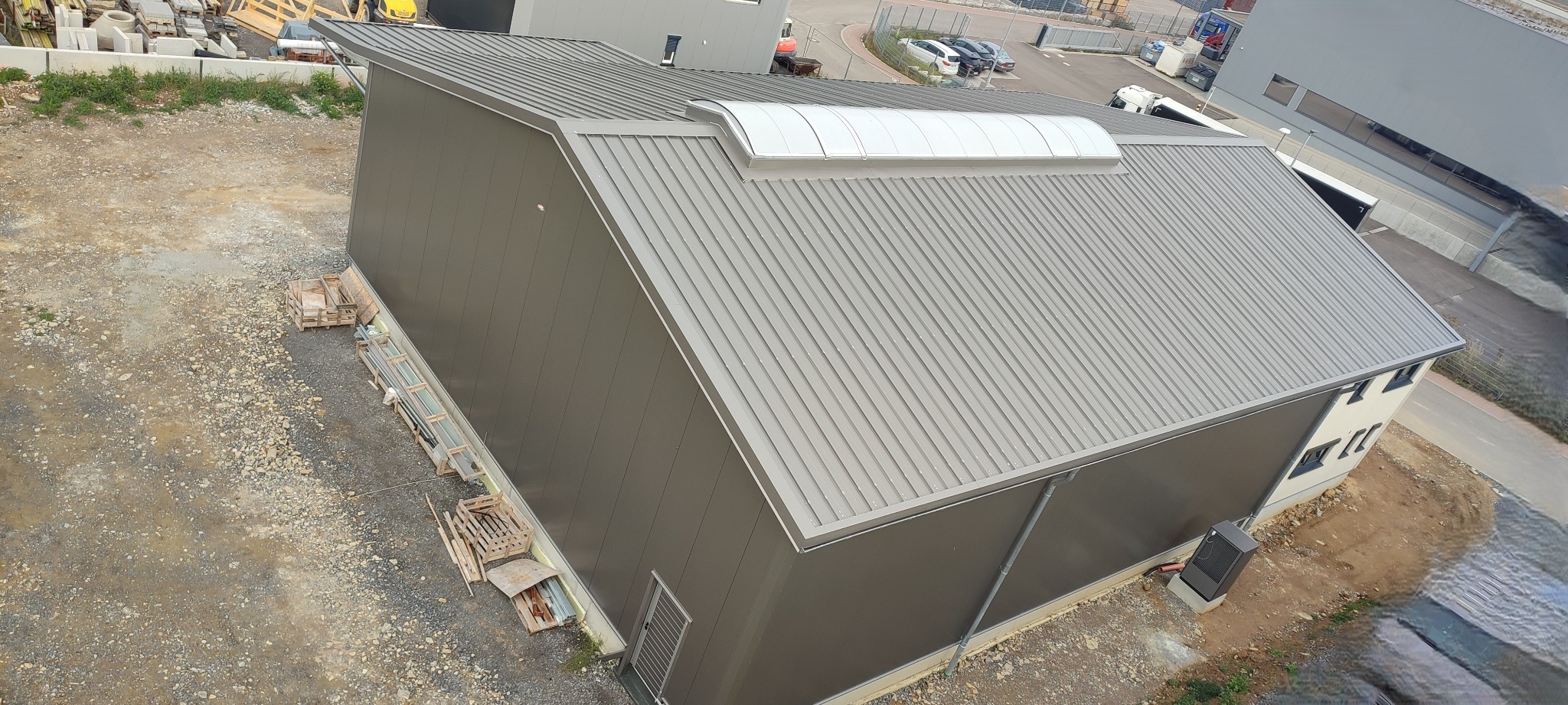 Nowoczesna hala przemysłowa z szarej płyty warstwowej i dachem z blachy trapezowej z świetlikiem, widok z góry.