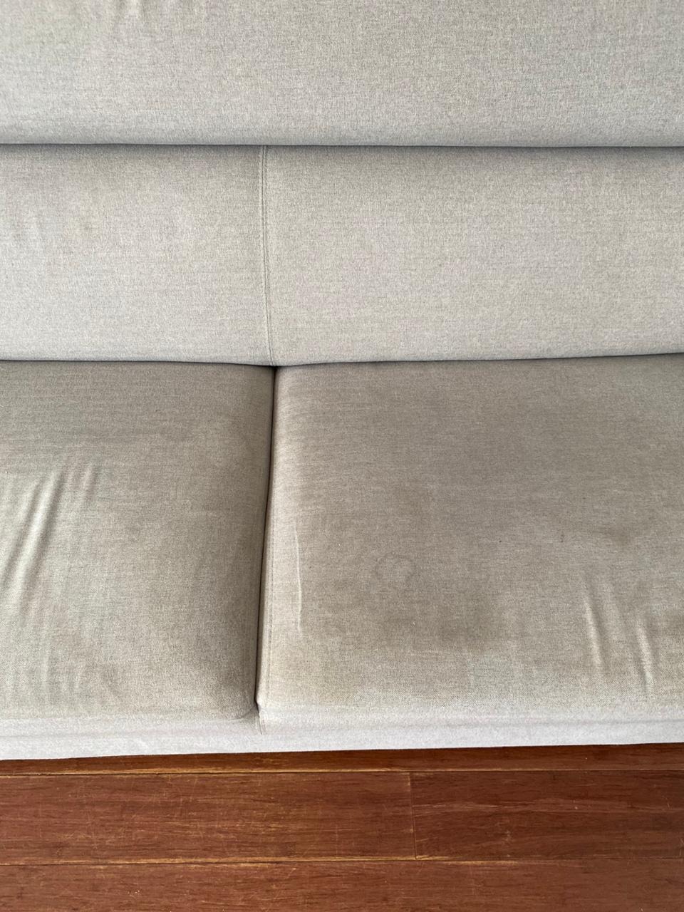Beżowa sofa z widocznymi plamami na siedzisku, drewniana podłoga w tle.