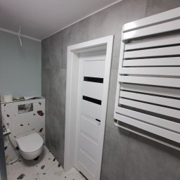 Julian paluch - Nowoczesna łazienka po remoncie: szare płytki ścienne, biała armatura, grzejnik drabinkowy i drzwi z czarnymi akcentami. Podłoga w stylu lastryko.