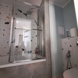 Julian paluch - Nowoczesna kabina prysznicowa z transparentnego szkła, zamontowana nad wanną w łazience wykończonej płytkami w stylu lastryko. Widoczna armatura i toaleta.