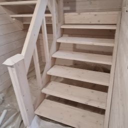 Łukasz - Jasne, drewniane schody z balustradą w domu o ścianach z boazerii. Widoczna puszka z farbą i folia ochronna na podłodze.
