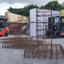Wytwórnia Materiałów Budowlanych Zdzisława Szczepańska - Szkielety zbrojeniowe z drutu zbrojeniowego na placu budowy, w tle wózki widłowe i palety z materiałami budowlanymi SOLBET i YTONG.