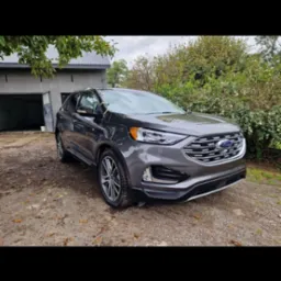 Szary Ford Edge po umyciu, stojący na żwirowym podjeździe przed garażem w pochmurny dzień.