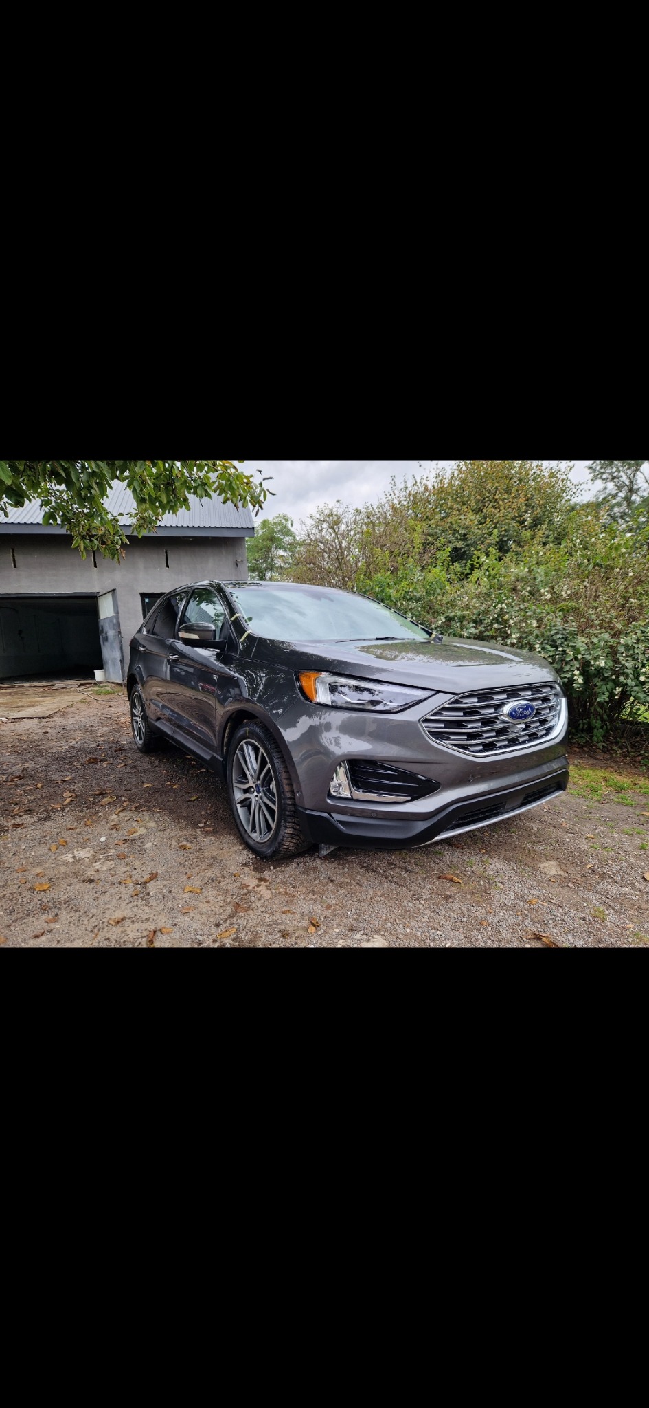 Szary Ford Edge po umyciu, stojący na żwirowym podjeździe przed garażem w pochmurny dzień.