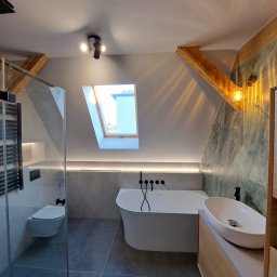 TIK BUD IVAN KIT - Nowoczesna łazienka na poddaszu z drewnianymi belkami, kabiną prysznicową typu walk-in, wolnostojącą wanną z czarną armaturą i umywalką nablatową na drewnianej szafce, oświetlona lampą z kloszem...