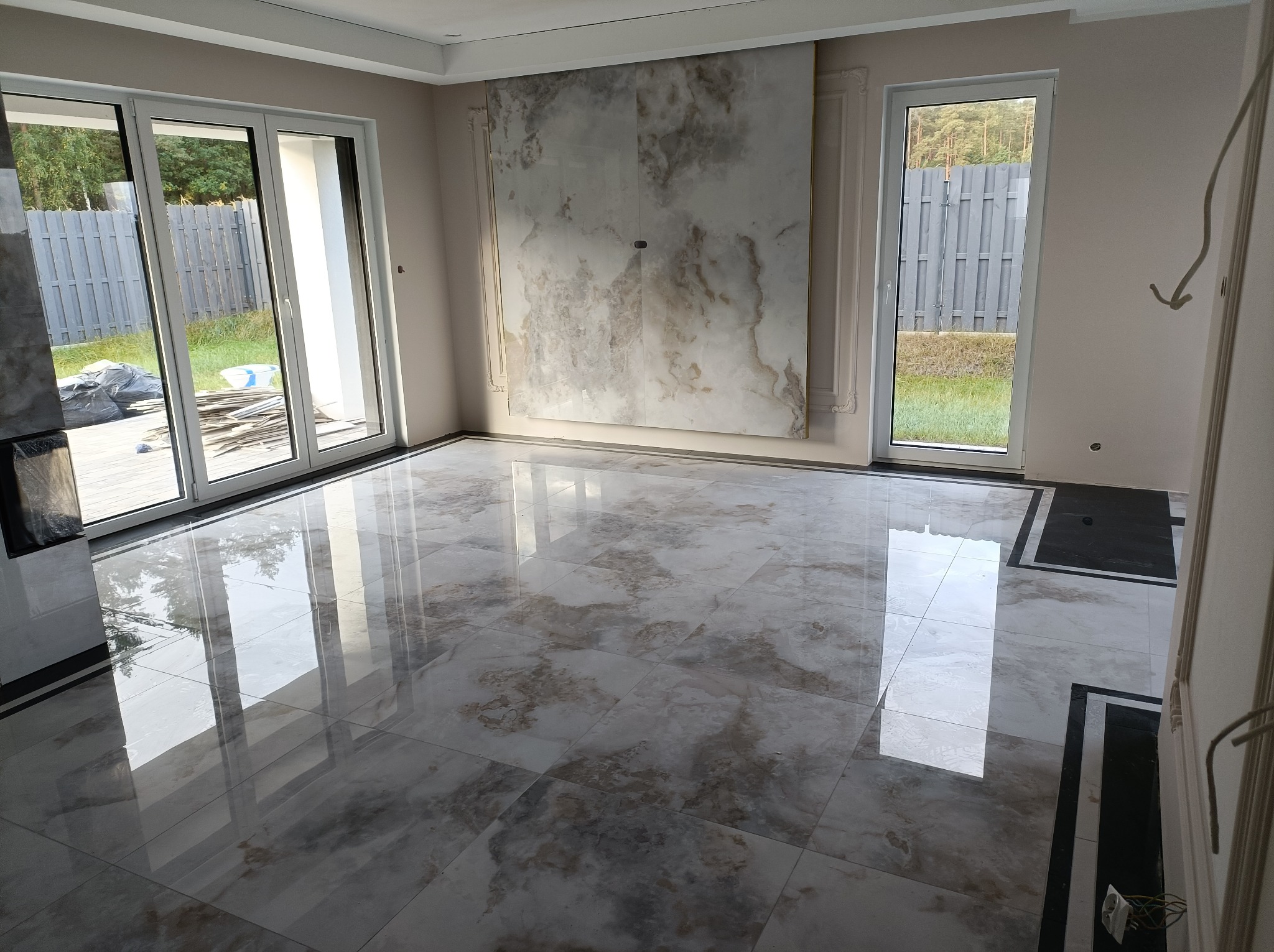 Błyszcząca, marmurkowa podłoga z płytek w nowym, jasnym pokoju z dużymi oknami i dekoracyjną ścianą z kamienia.