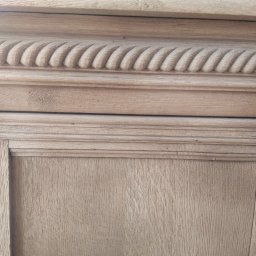 Wiktor Kawa - Fragment drewnianej szafki z dekoracyjnymi frezami i toczonym elementem kolumny, widoczna struktura drewna i ślady po gwoździach.