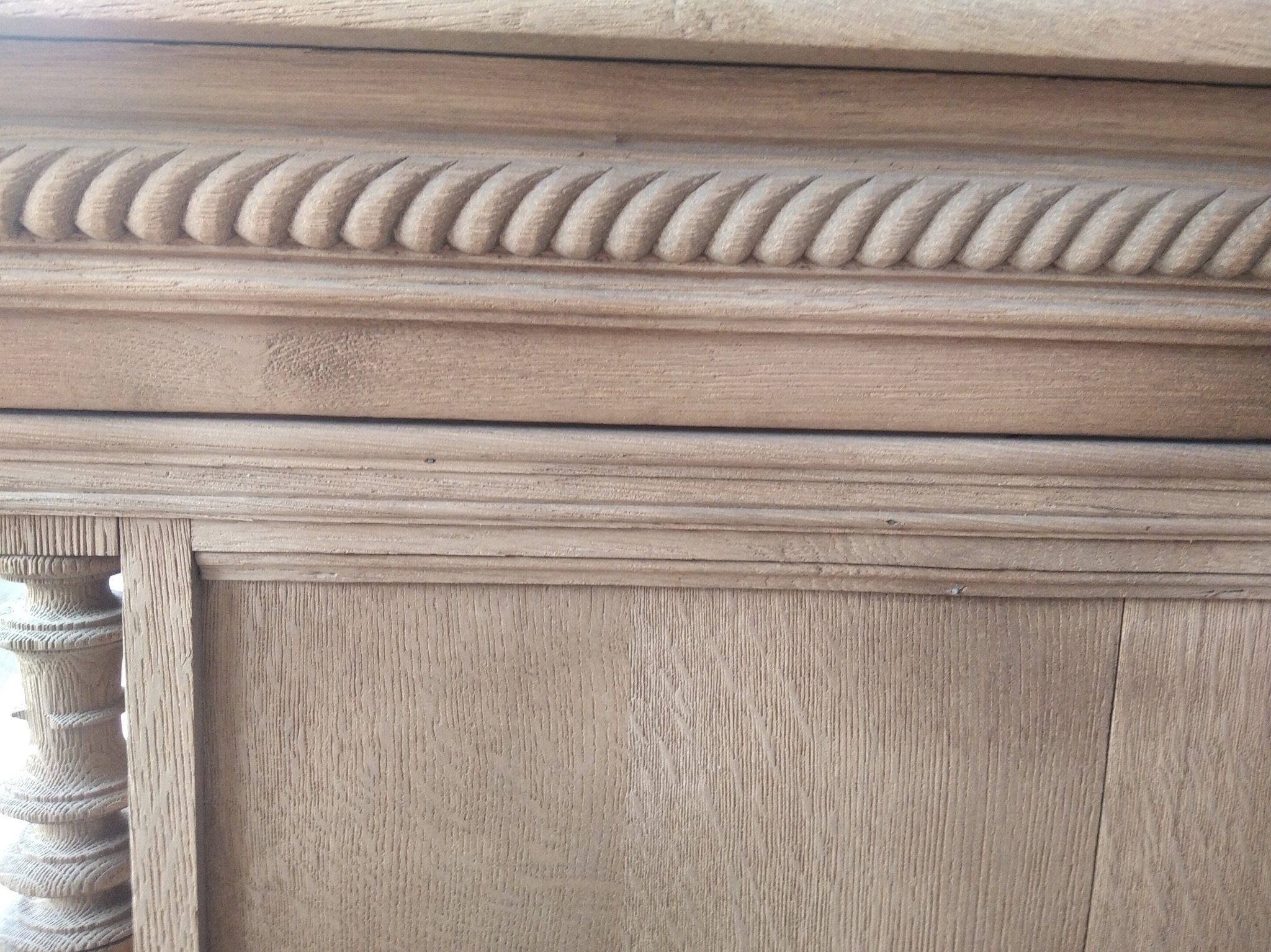 Fragment drewnianej szafki z dekoracyjnymi frezami i toczonym elementem kolumny, widoczna struktura drewna i ślady po gwoździach.