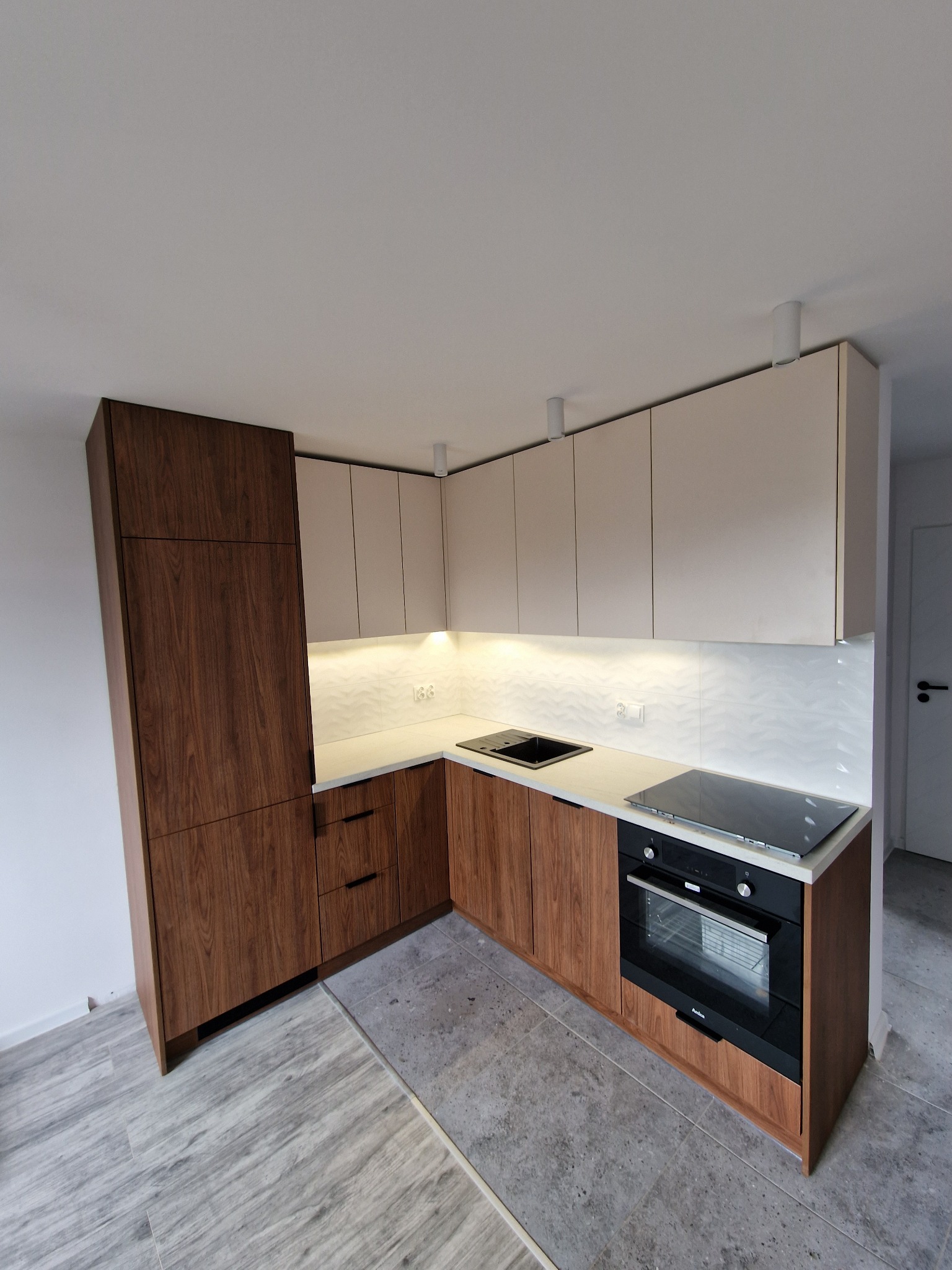 Nowoczesna kuchnia w kształcie litery L z drewnianymi dolnymi szafkami i jasnymi górnymi, oświetlona listwą LED pod szafkami, z płytą indukcyjną i piekarnikiem w zabudowie.