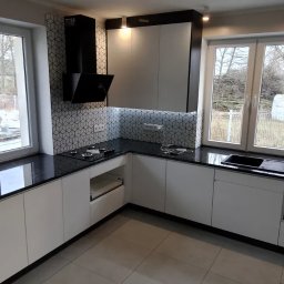 Zakład Kamieniarski Wojciech Lociński - Nowoczesna kuchnia z czarnym blatem i białymi szafkami, widoczne okno z widokiem na zewnątrz, płytki w geometryczny wzór na ścianie.