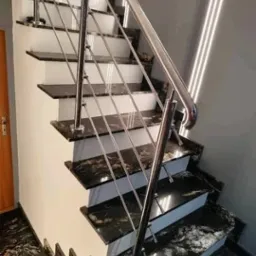 Schody wewnętrzne z czarnego, polerowanego kamienia z widocznym użyleniem, zabezpieczone balustradą ze stali nierdzewnej z cienkimi, poziomymi prętami.