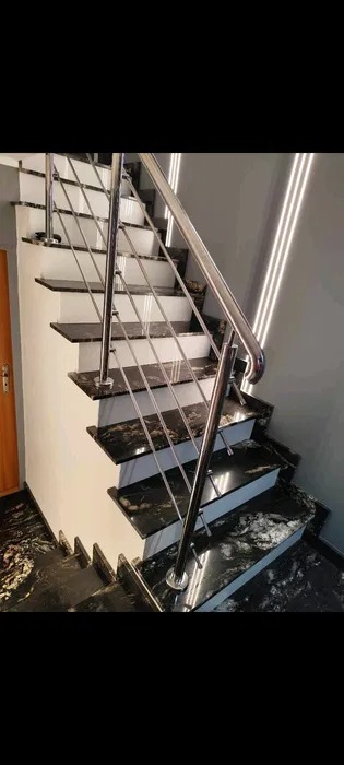 Schody wewnętrzne z czarnego, polerowanego kamienia z widocznym użyleniem, zabezpieczone balustradą ze stali nierdzewnej z cienkimi, poziomymi prętami.