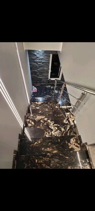 Wewnętrzne schody z czarnego kamienia z jasnymi, nieregularnymi wzorami, wykończone metalową balustradą i oświetleniem LED wzdłuż ściany.