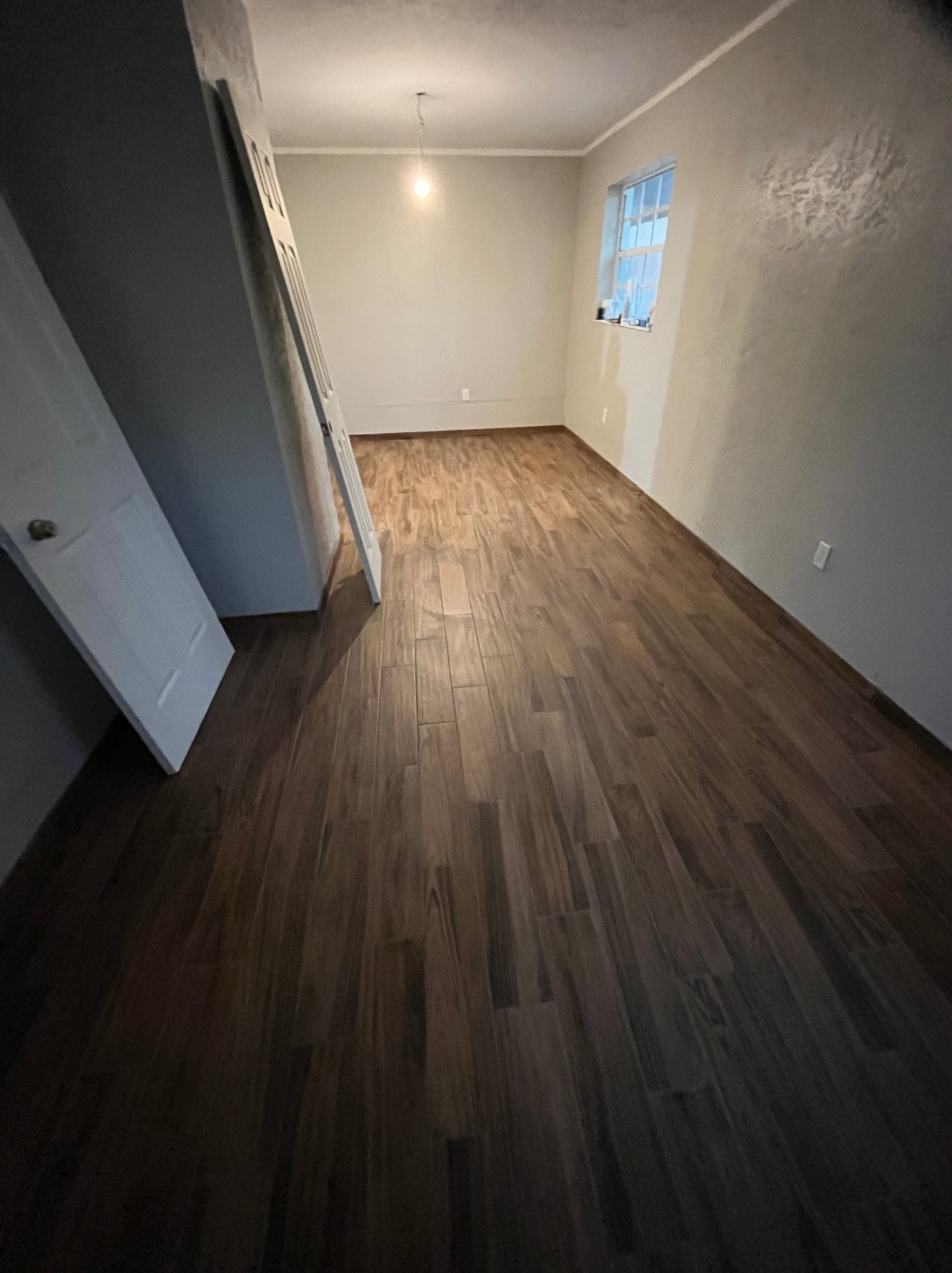 Wykończone wnętrze pokoju z ułożoną podłogą z paneli imitujących drewno. Widoczne białe ściany i okno z firanką. Drzwi opierają się o ścianę.