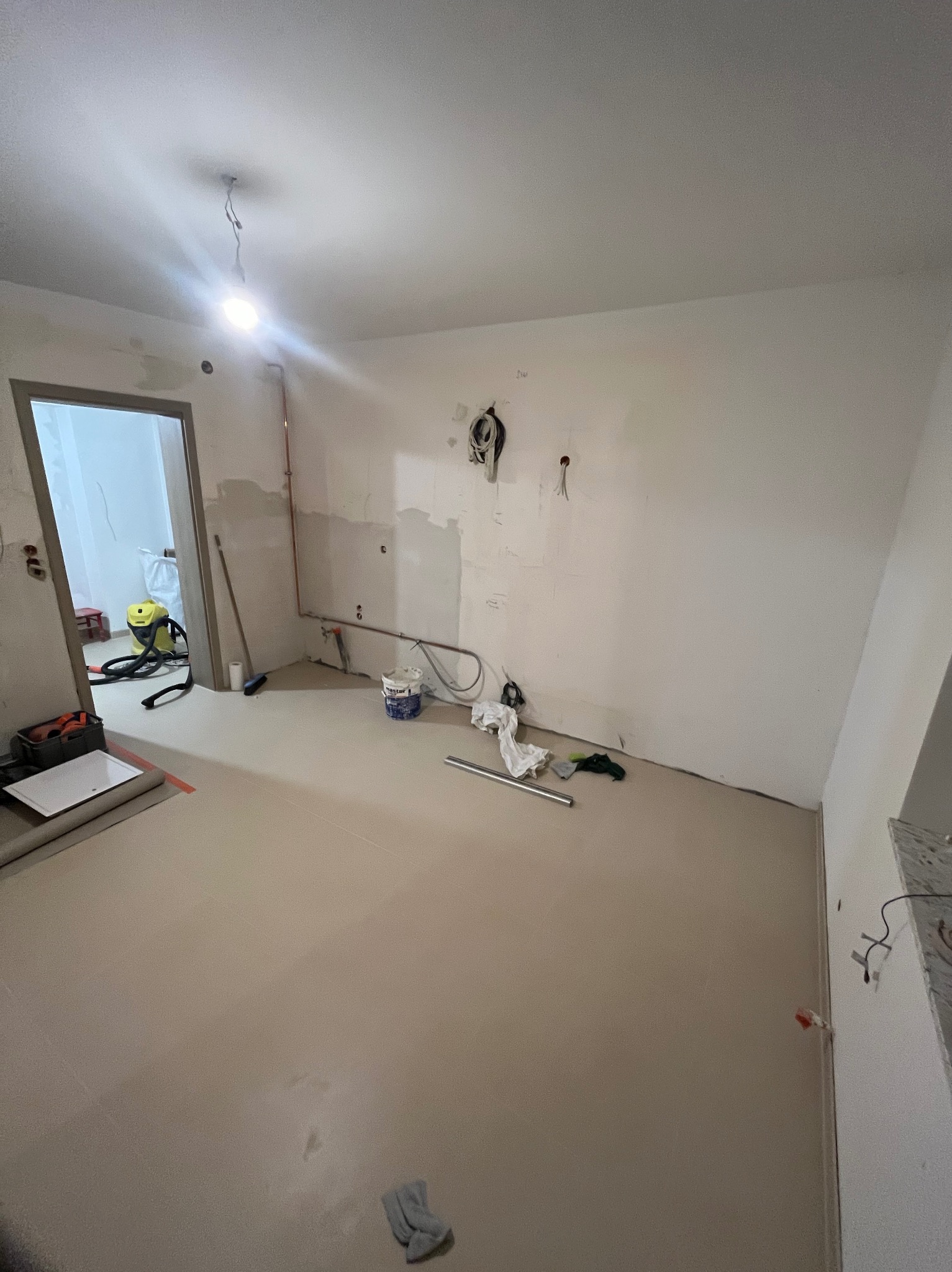 Wnętrze w trakcie prac wykończeniowych: widoczne instalacje, ślady po szpachlowaniu, narzędzia i akcesoria. Podłoga zabezpieczona, gotowa do dalszych prac.