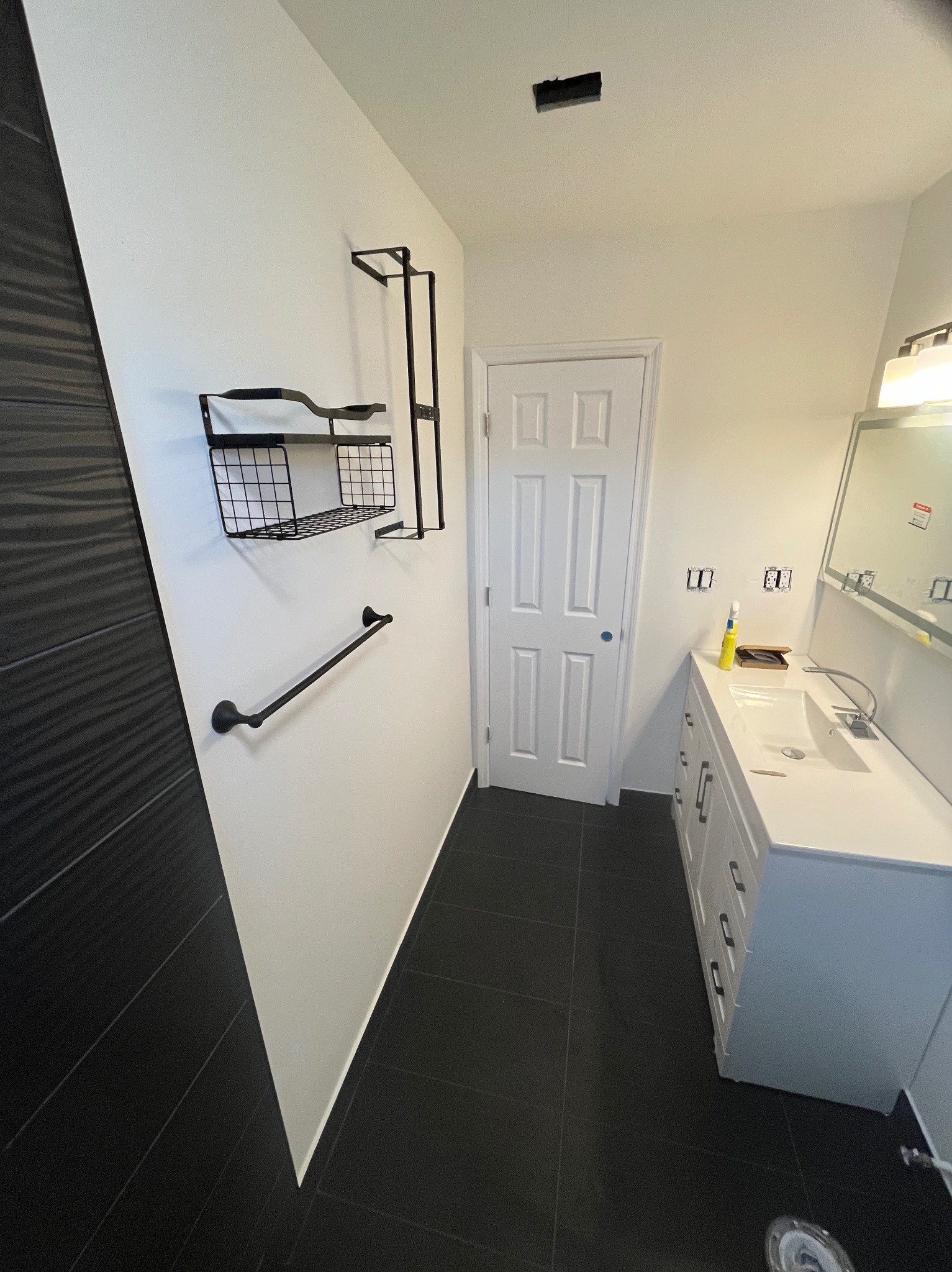 Nowoczesna łazienka z czarno-białymi płytkami, czarnymi akcesoriami i białą szafką z umywalką. Widoczne przygotowania do montażu osprzętu elektrycznego.