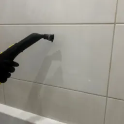 Czyszczenie parowe płytek w łazience przy użyciu parownicy Kärcher, widoczna ręka w czarnej rękawicy, białe płytki i fragment wanny.