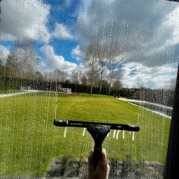 Czyste Wnętrze Magdalena Dykalska - Mycie okna z widokiem na ogród. Na szybie piana i ślady po ściągaczce Unger ErgoTec Ninja, w tle trawnik, drzewa i meble ogrodowe.