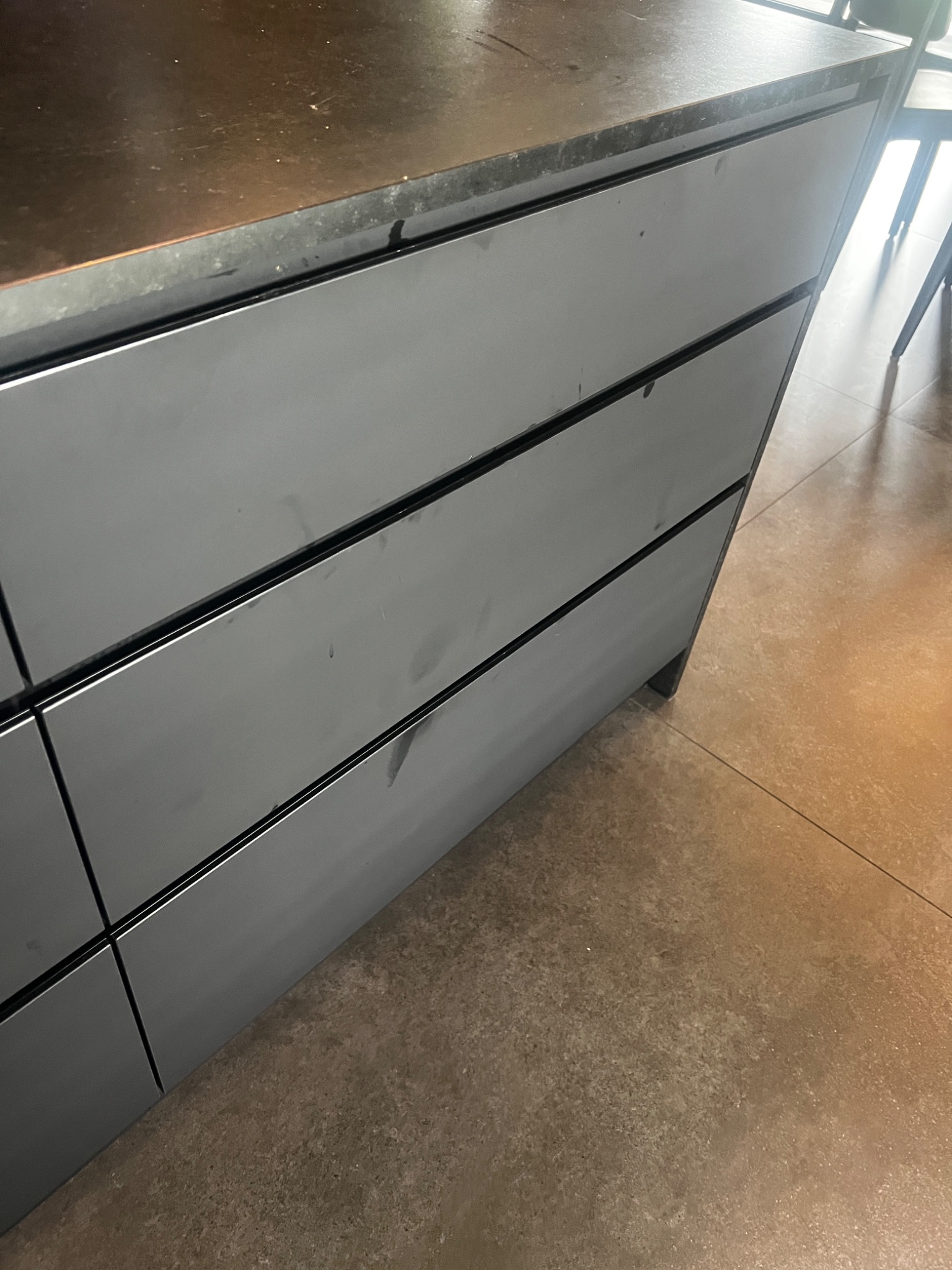 Szare, matowe fronty szafek kuchennych z widocznymi plamami i zaciekami, wymagające dokładnego czyszczenia. Na blacie widoczne zabrudzenia.